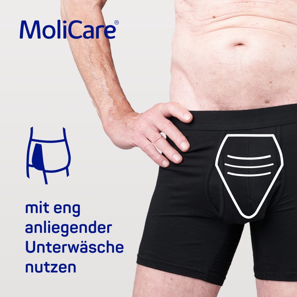 Ein MoliCare Premium Men Pad wird auf einer neutralen Unterlage dargestellt. Das Produkt ist in einer Packung zu sehen, die dem Benutzer zeigt, wie die Einlage angelegt wird. Um die Verpackung herum sind Hinweise auf die Produkteigenschaften vermerkt, darunter Saugfähigkeit und Diskretion. Im Hintergrund ist unscharf der Hinweis auf die anliegende Unterwäsche zu erkennen, was die Anwendung des Pads verdeutlicht.