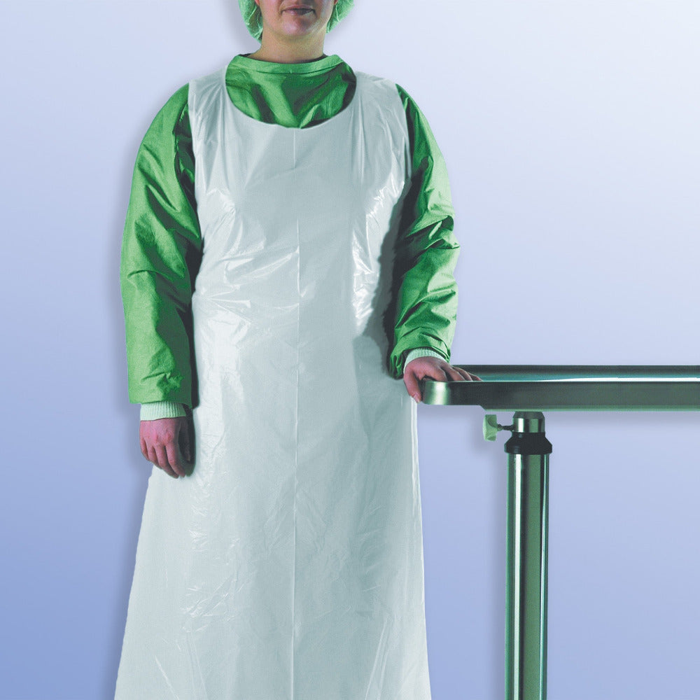 Person in grüner OP-Kleidung trägt eine weiße Schutzschürze von Dahlhausen aus Kunststoff, stehend vor einem medizinischen Edelstahltisch.