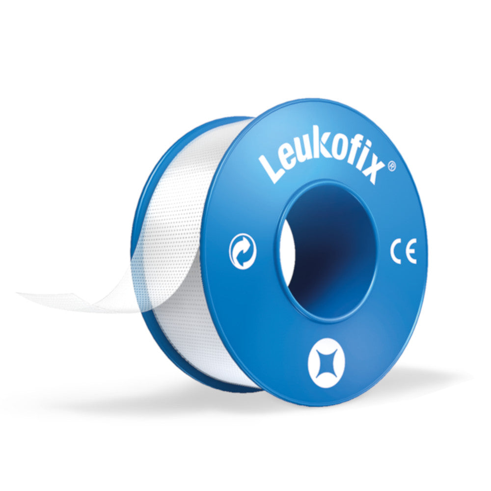 Transparente Leukofix Pflasterrolle auf einem hellen Hintergrund. Die Verpackung zeigt eine rote und blaue Farbgebung mit dem Schriftzug „Leukofix transparent“ gut lesbar auf der Vorderseite. Die Rolle ist teilweise entfaltet, was die darum gewickelte, transparente Pflasterfolie sichtbar macht. Die Ränder des Pflasters sind sauber und die Oberfläche glänzend. Ideal für dieFixierung von Verbänden oder Sensoren auf der Haut.