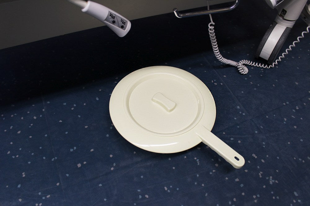 Runde Bettpfanne aus robustem Kunststoff, ideal für den Einsatz im Pflegebereich. Die Pfanne ist in einem klaren, hygienischen Weiß gehalten und verfügt über einen passenden Deckel, der eine einfache und sichere Aufbewahrung ermöglicht. Die Oberfläche ist glatt und leicht zu reinigen, was eine hygienische Nutzung unterstützt. Die ergonomische Form sorgt für Komfort und Praktikabilität, während die stabilen Griffe eine einfache Handhabung gewährleisten.