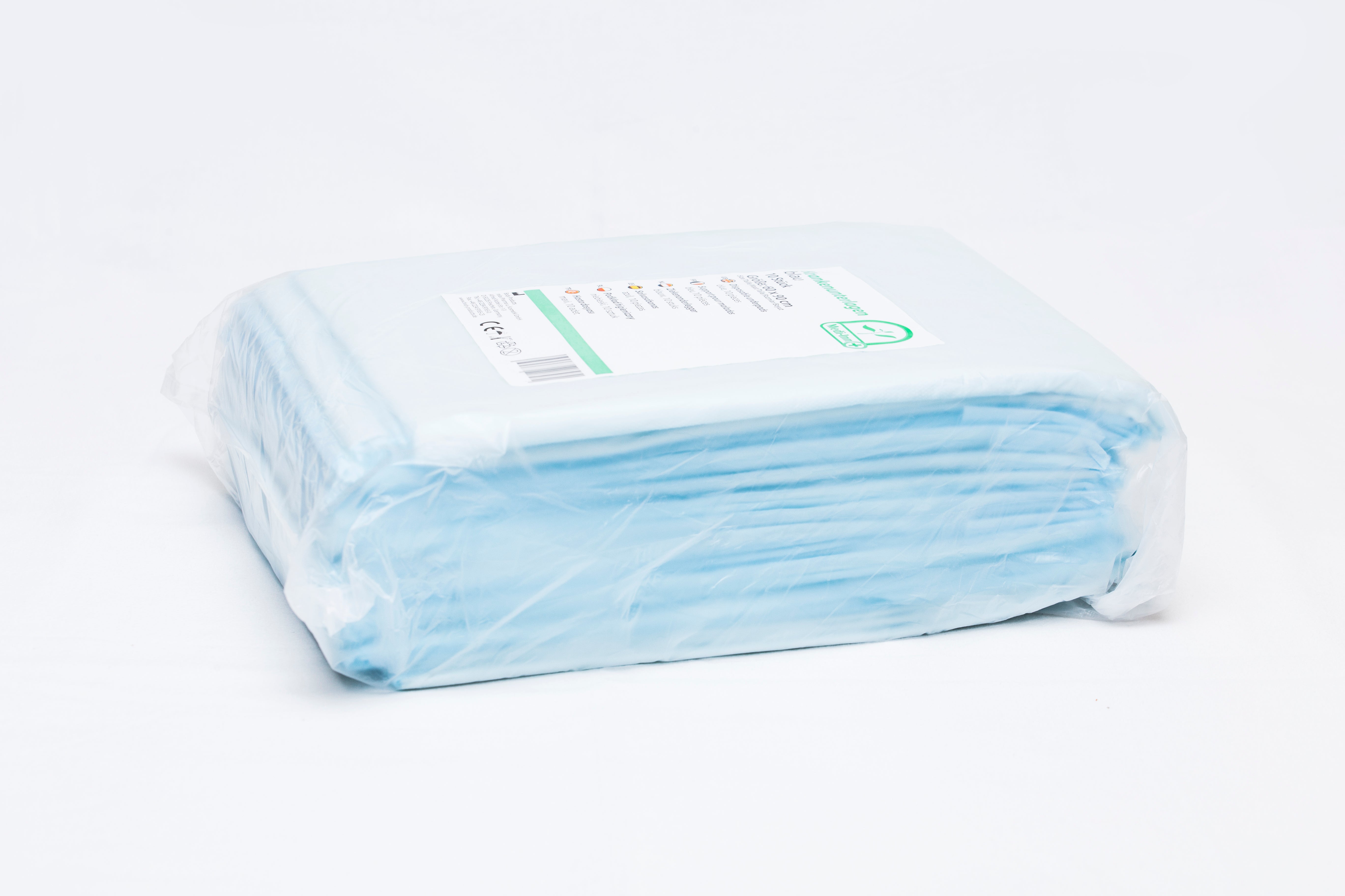 Ein Paket mit 6-lagigen Einmalunterlagen in der Größe 60 x 90 cm, die auf einem weißen Hintergrund liegen. Die Unterlagen sind in einem erkennbaren blauen Design mit einem strukturierten, wasserabweisenden Obermaterial. Die Verpackung ist transparent, wodurch die einzelnen Unterlagen sichtbar sind. In der oberen rechten Ecke befindet sich ein Etikett mit Produktinformationen.