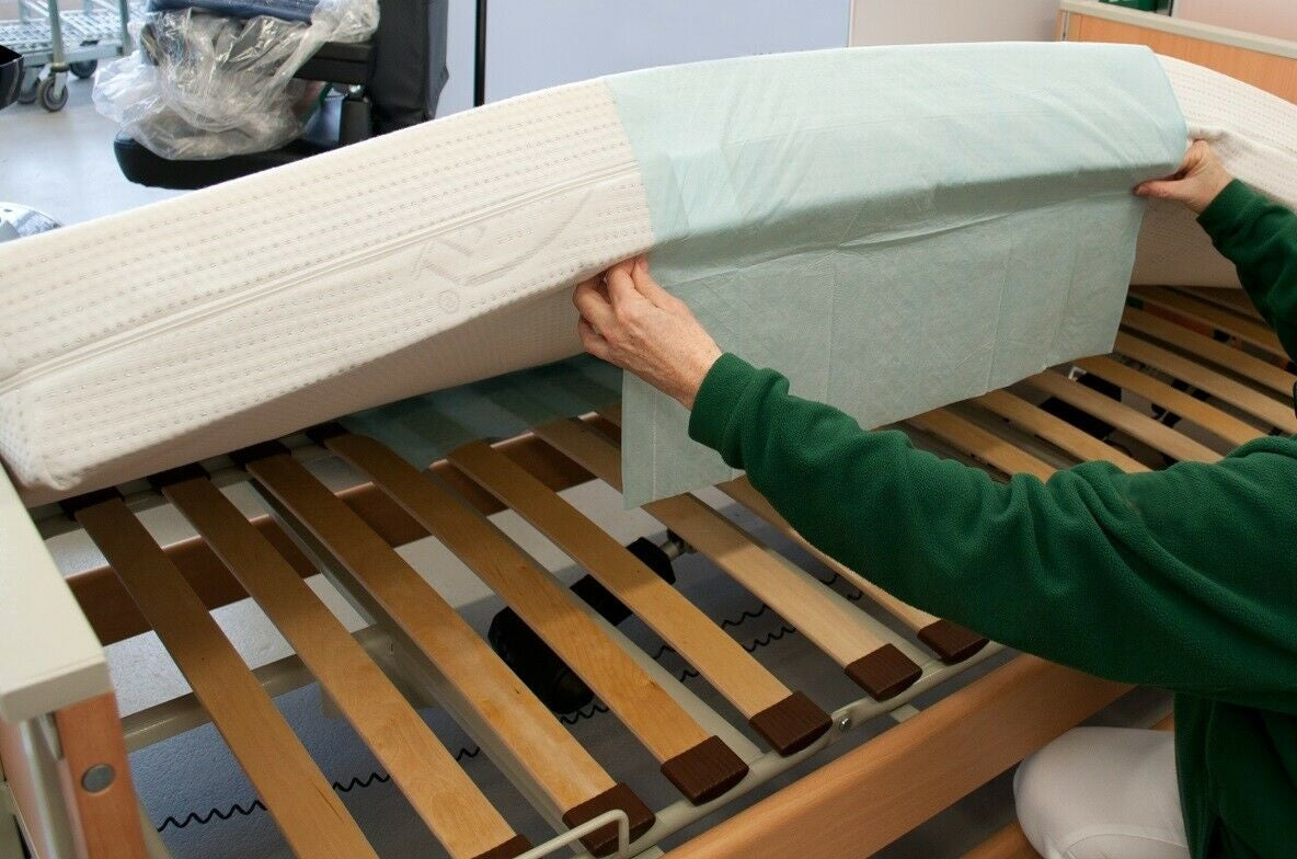 Bildbeschreibung eines Produkts: Medi Inn Krankenunterlagen SAP Plus Premium mit den Maßen 70 x 175 cm. Die Unterlagen sind in einem frischen, weißen Hintergrund präsentiert. Die Oberfläche wirkt glatt und strapazierfähig. An der Unterkante des Bildes sind einige Verpackungen zu sehen, was auf eine praktische innerbetriebliche Verwendung hinweist.