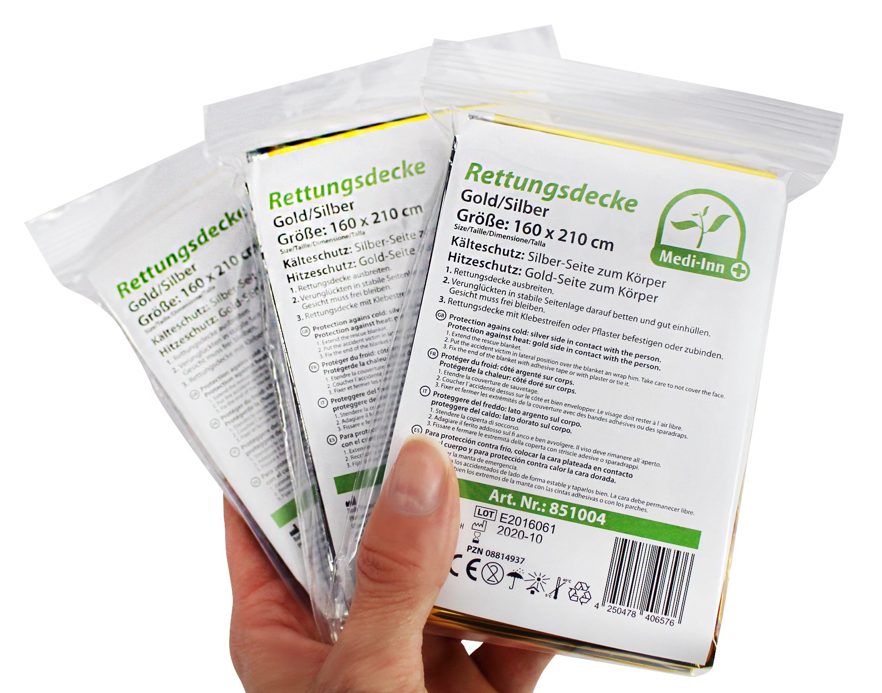 Ein Querformat-Bild zeigt eine Rettungsdecke aus glänzendem, reflektierendem Material, das auf einer neutralen Oberfläche ausgebreitet ist. Die Decke ist in zwei Hälften unterteilt: eine Seite ist in goldener Farbe und die andere in silberner Farbe. Das Material der Decke wirkt leicht und dünn, aber dennoch stabil. An den Rändern sind die Konturen gut sichtbar, die die rechteckige Form der Decke unterstreichen. Im Hintergrund ist unscharfes, neutrales Licht zu sehen, das die Farben der Decke hervorhebt.