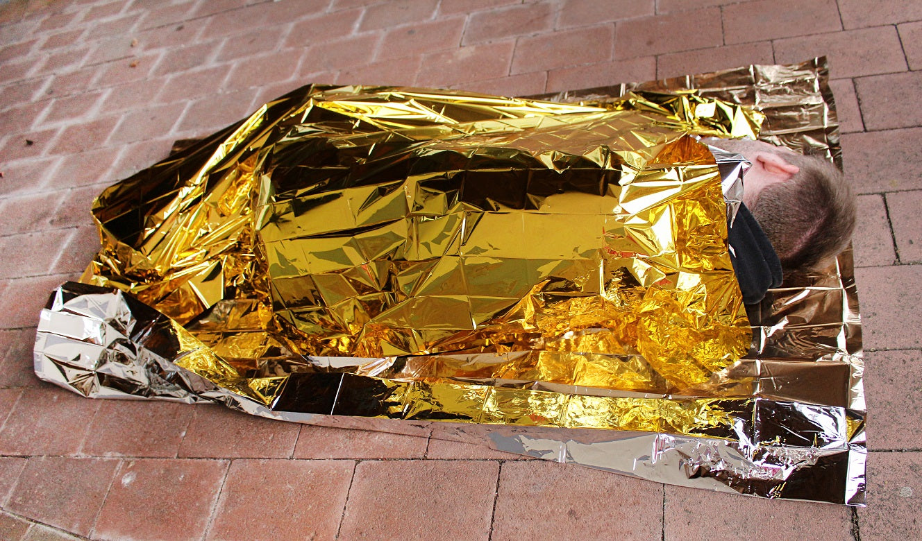 Eine Rettungsdecke in Gold und Silber, die auf einem neutralen Hintergrund präsentiert wird. Die Decke misst 160 x 210 cm und ist einseitig in glänzendem Gold und auf der anderen Seite in silberner Reflexion gestaltet. Dies macht sie ideal für Notfälle, um Körperwärme zu speichern oder als Sichtschutz zu dienen. Die Falten und Linien der Decke zeigen ihre Flexibilität und Robustheit.