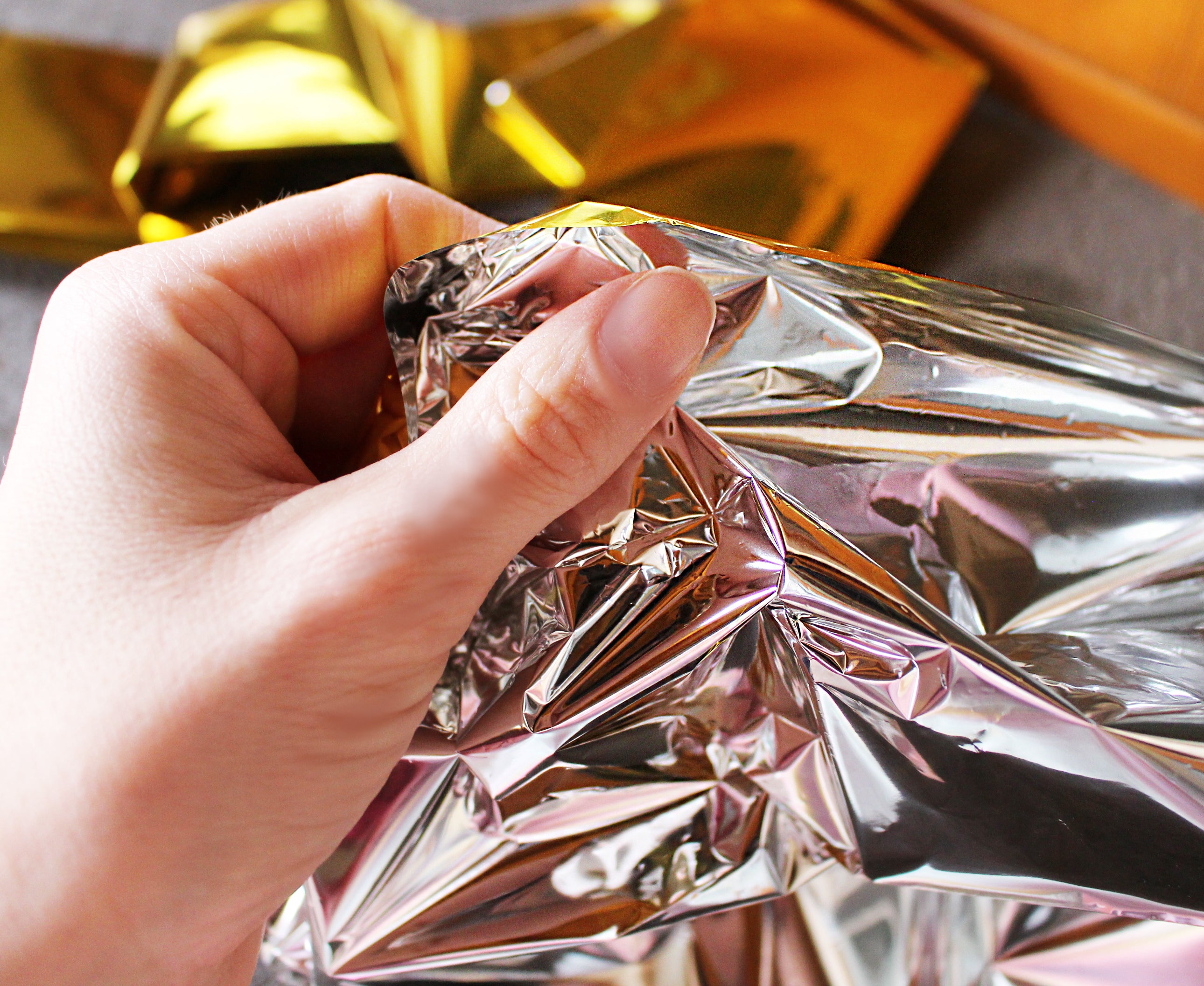 Eine Rettungsdecke in Gold- und Silber-Optik liegt auf einem weißen Hintergrund. Die Decke hat eine rechteckige Form und misst 160 x 210 cm. Ihre Oberfläche reflektiert Licht, was einen glitzernden Effekt erzeugt. Eine Seite ist in Gold, die andere in Silber gehalten, wodurch sie vielseitig einsetzbar ist. Die Decke ist faltbar und flexibel, geeignet für Notfälle, Outdoor-Aktivitäten oder als Isolationshilfe.