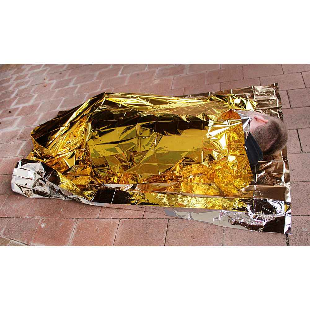 Bild zeigt eine Rettungsdecke in gold-silberner Farbgestaltung, die auf einer hellen Oberfläche ausgebreitet ist. Die Decke misst 160 x 210 cm und ist in zwei Hälften geteilt: eine Seite reflektiert warmes Licht in Gold, während die andere Seite in silbernem Farbton leuchtet. Die glänzende Oberfläche sorgt für einen hohen Reflexionsgrad. Die Decke eignet sich optimal für Notfälle, Wärmeisolierung und Outdoor-Aktivitäten.
