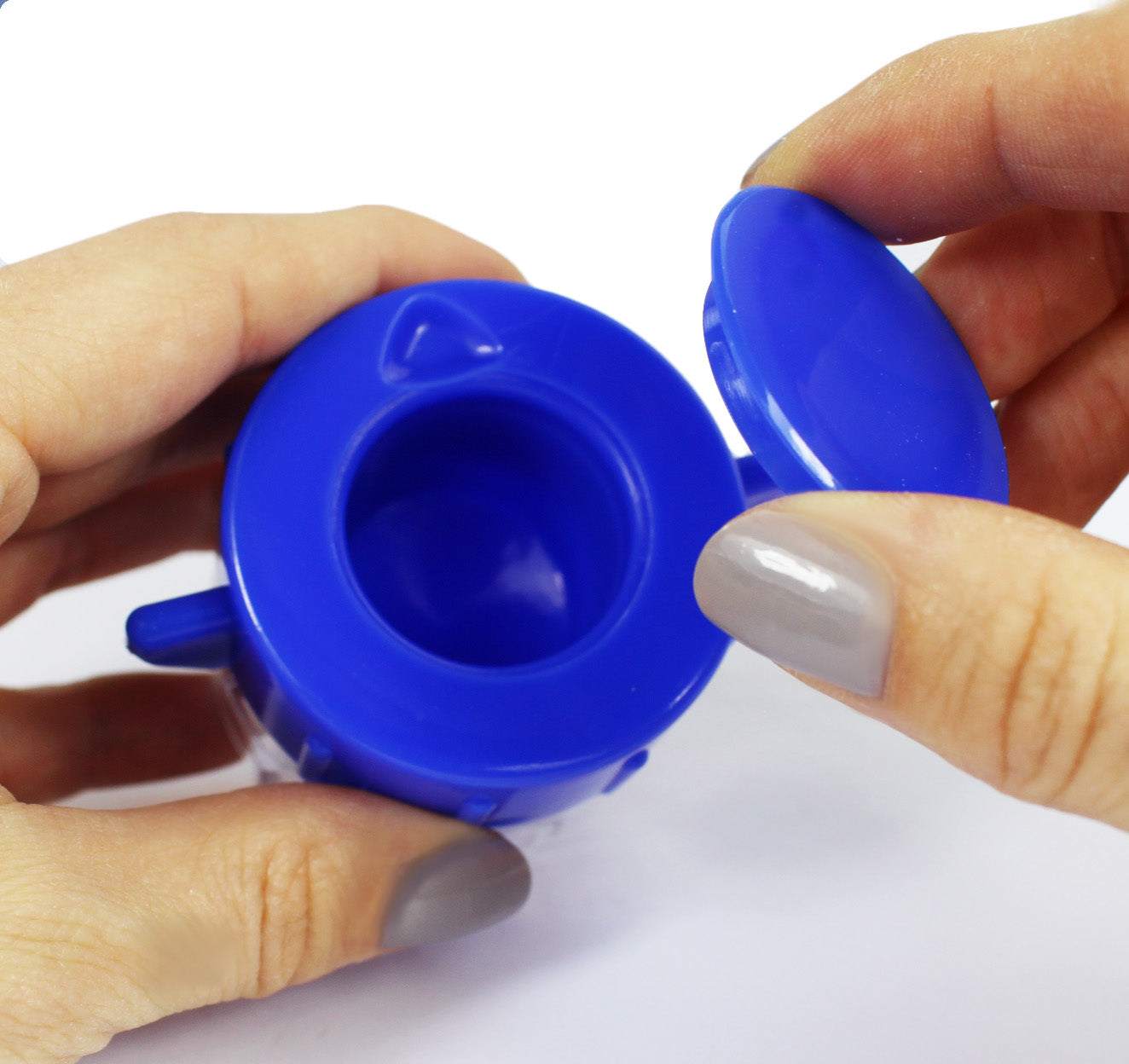 Ein blauer Tablettenmörser mit einem transparenten Medikamentenfach steht auf einer weißen Unterlage. Der Mörser hat einen konischen Körper mit einer feinen, glatten Oberfläche und einen breiten, festen Boden, der Stabilität bietet. Oben befindet sich ein passender Deckel, der das Medikamentenfach sicher verschließt. Im Hintergrund ist eine unscharfe, neutrale Umgebung zu sehen, die den Fokus auf den Mörser legt.