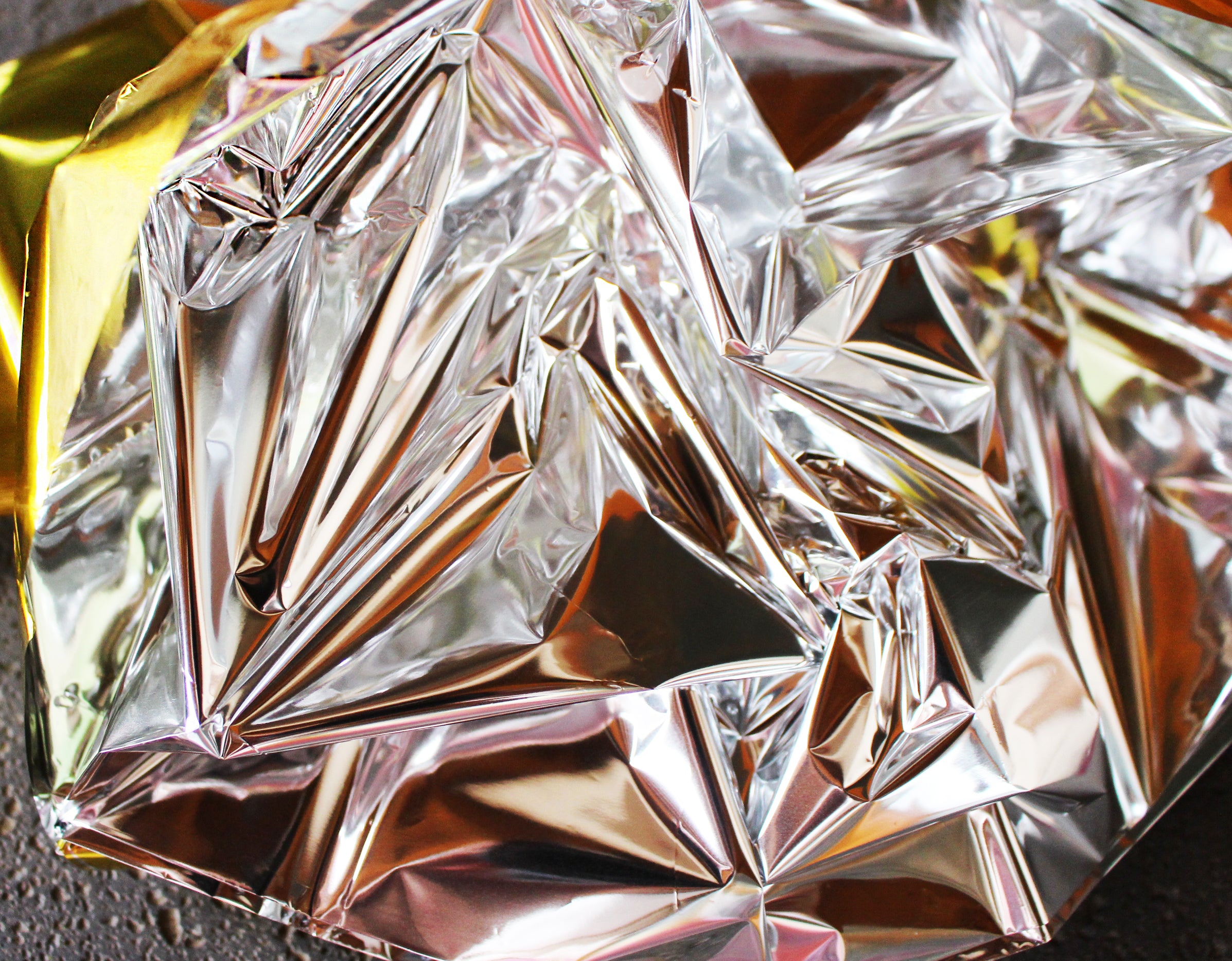Bildbeschreibung: Das Bild zeigt eine Packung mit zwei Rettungsdecken in den Farben Gold und Silber. Jede Decke hat die Abmessungen von 1,6 m x 2,1 m und ist platzsparend gefaltet, um die Handhabung zu erleichtern. Der goldene und silberne Farbton reflektiert Licht und sorgt für eine effektive Wärmeregulierung. Im Hintergrund des Bildes ist ein unscharfer, neutraler Untergrund zu sehen, der die Aufmerksamkeit auf die Rettungsdecken lenkt.