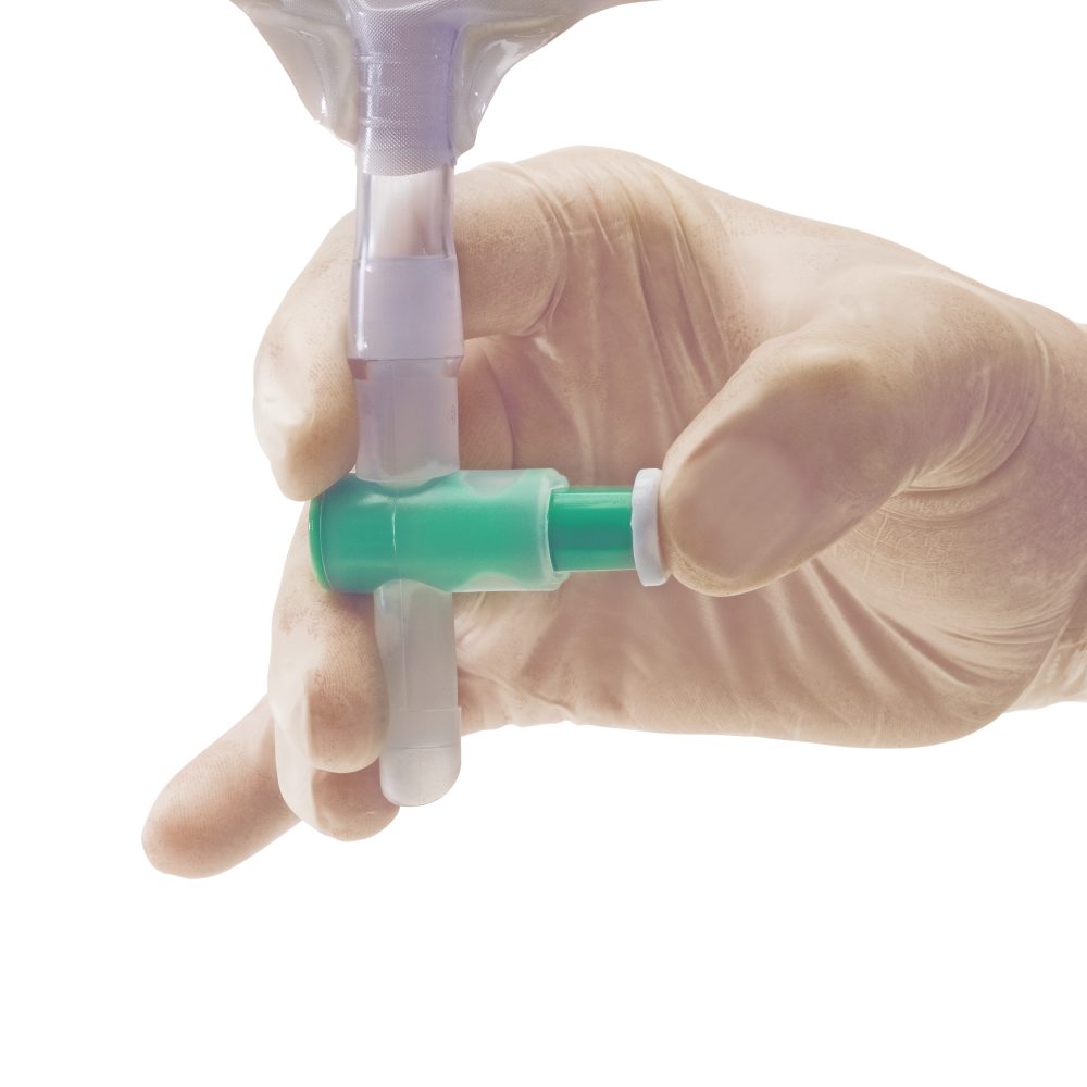 Ein Ureofix 112 Plus Urindrainagebeutel mit einem Fassungsvermögen von 2000 ml ist abgebildet. Der transparente Beutel zeigt eine Graduierung zur einfachen Flüssigkeitskontrolle. Er hat einen 110 cm langen Schlauch, der zur sicheren Anwendung und Verbindung dient. In der unteren rechten Ecke des Bildes sind ein Paar Einmalhandschuhe zu sehen, die für hygienische Handhabung des Beutels gedacht sind. Der Hintergrund ist neutral gehalten, um die Details des Beutels und der Handschuhe hervorzuheben.
