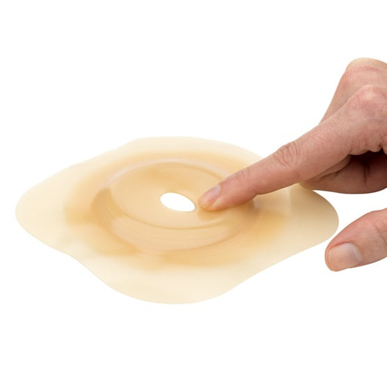 Quadratische, transparente Verpackung mit einer medizinischen Basisplatte für Stomaanpassungen. Die Basisplatte hat eine konvexe Form und ist mit einer klaren Schutzfolie versehen. Auf der Oberseite ist das Logo von Dansac sichtbar. In der Ecke befindet sich die Artikelbezeichnung „Nova 2 Basisplatte convex RR55“ sowie die Größenangabe „15-42mm“. Die Verpackung zeigt eine ordentliche, saubere Gestaltung und spricht professionelle Nutzer an, die hochwertige Produkte im Bereich der Stomaversorgung suchen.
