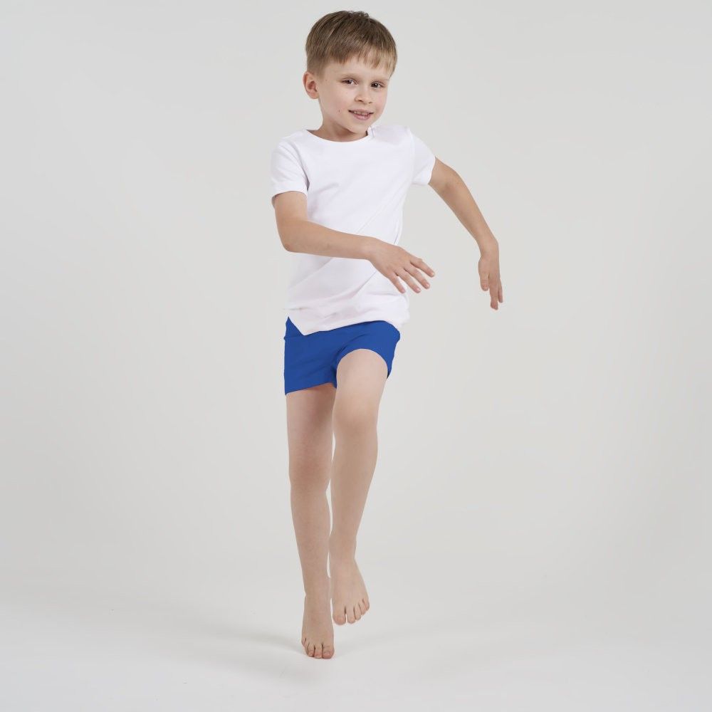 Kind läuft auf die Kamera zu, trägt weiße ActivePants mit blauer Hose, freudiger Gesichtsausdruck.